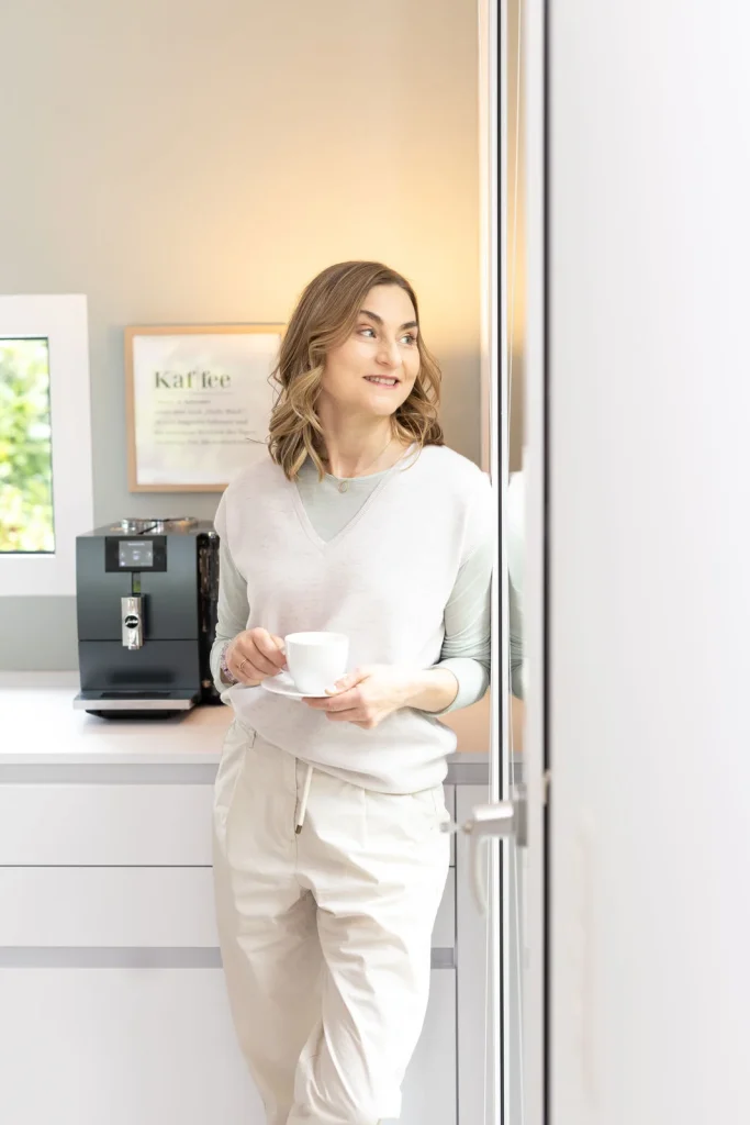 Patricia Myriam mit Kaffeetasse – achtsamer Moment der Reflexion in lichtdurchflutetem Raum