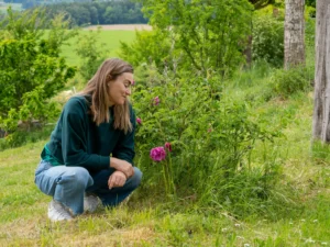 Frau vor einem kleinen Rosenbusch inmitten von safigem Grün im Mai